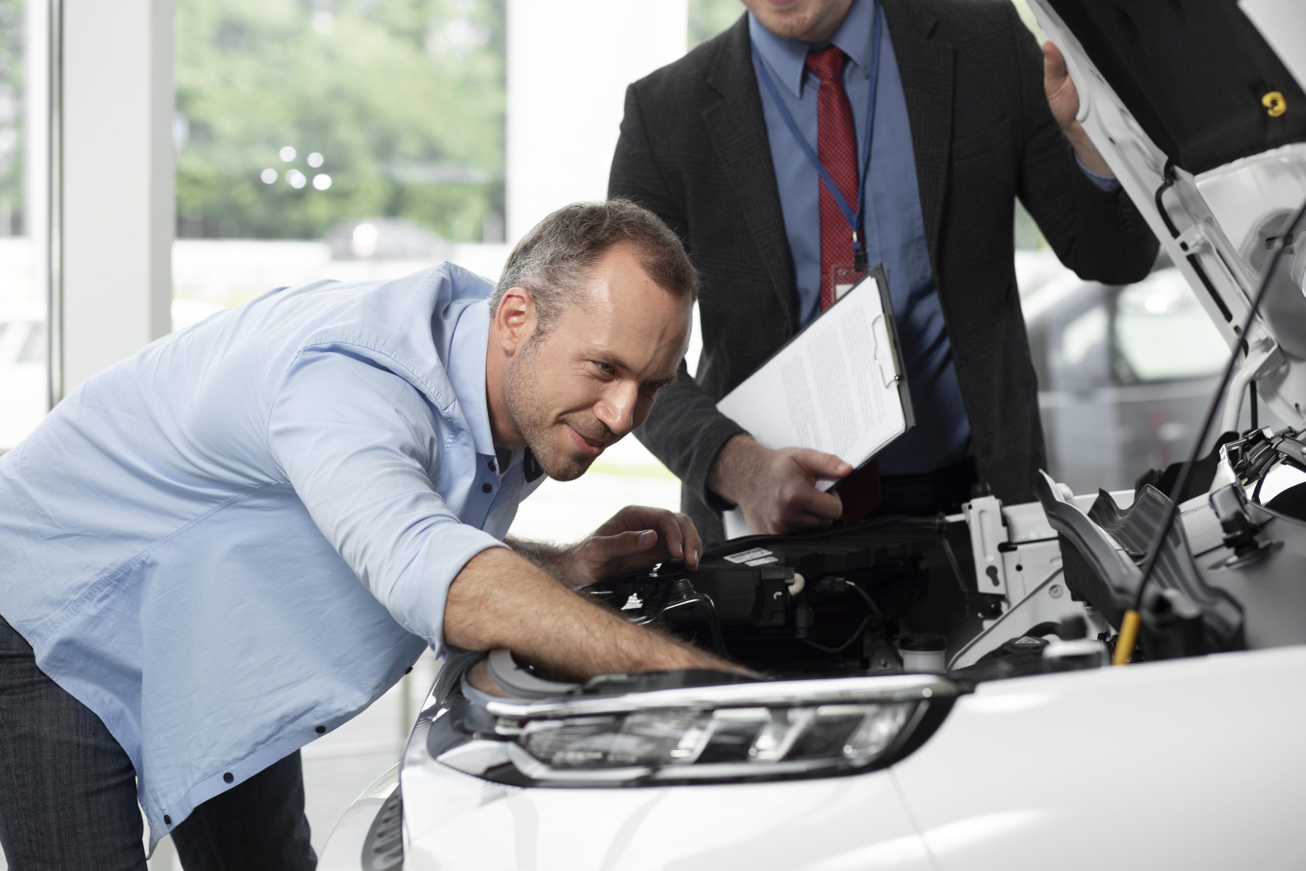 Customer and service advisor inspecting a vehicle engine at a dealership