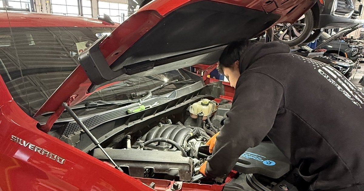 Jupiter Chevrolet technician inspecting the coolant reservoir on a red Chevrolet Silverado in the Garland, TX service bay